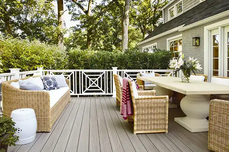 A deck with an outdoor living room with a modern dining table and chairs on one side and a wicker couch on the other side. The deck was built with gray deck boards.