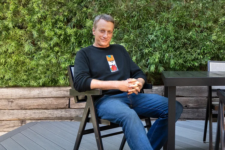 Tony Hawk gently smiles with folded hands sitting in a chair on his new deck.