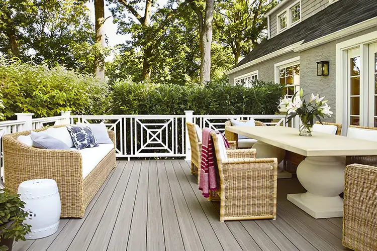 A deck with an outdoor living room with a modern dining table and chairs on one side and a wicker couch on the other side. The deck was built with gray deck boards.